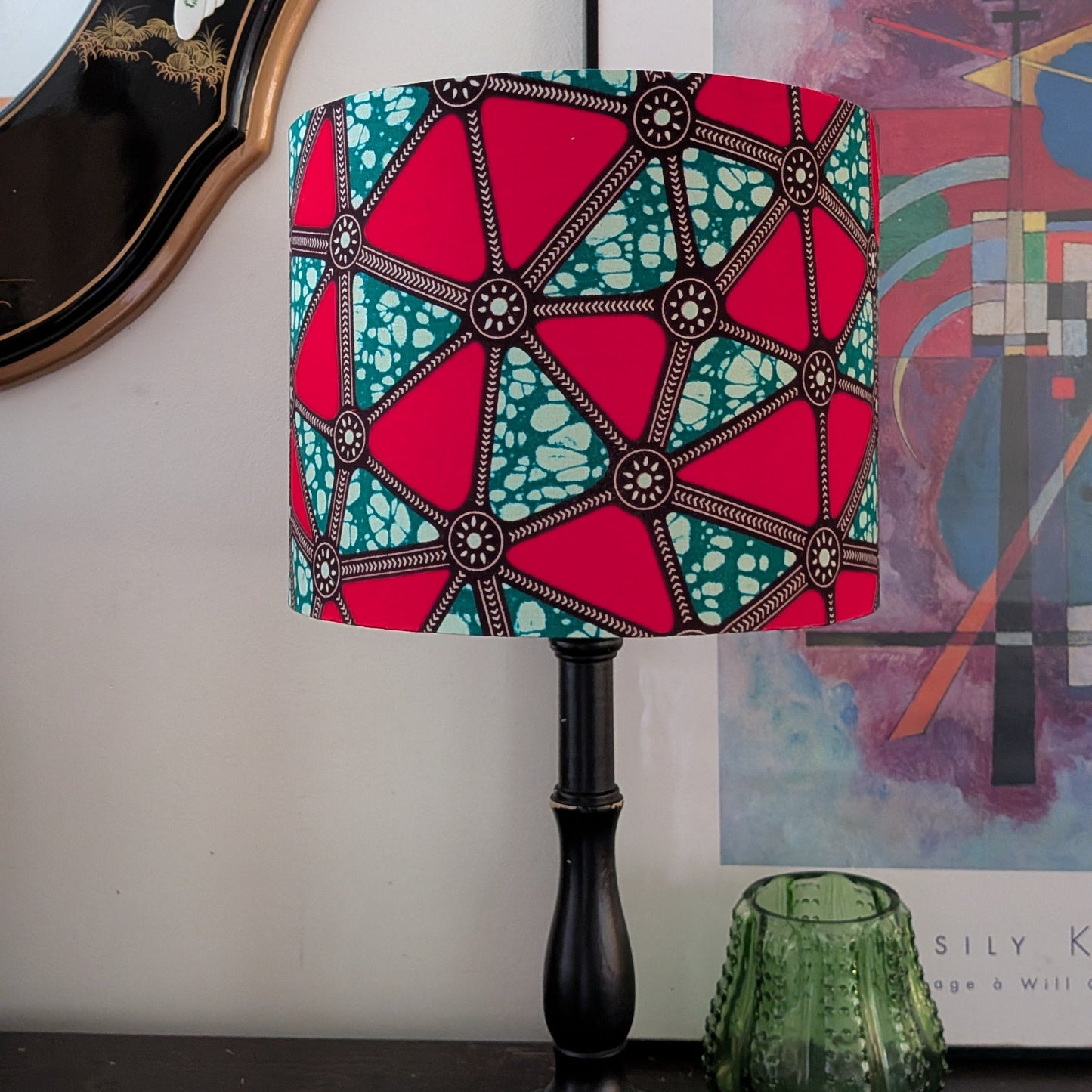 Decorative lamp with geometric red and green watermelon triangles shade on a table next to a framed picture.