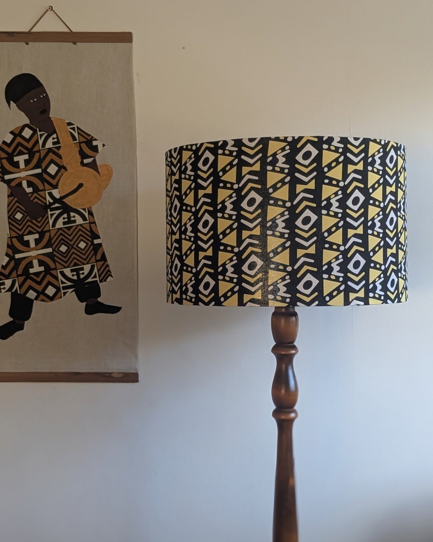 Lamp with a patterned shade next to a wall with a framed picture of an African drummer man.