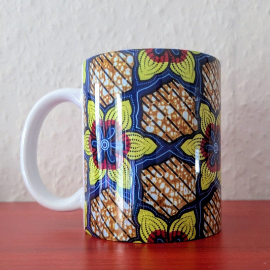 A white African print ceramic mug with a yellow red blue daisy  pattern. It has  a glossy finish. 