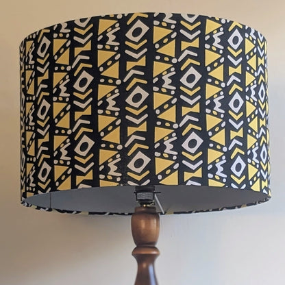 A patterned drum lampshade on a wooden stand against a plain background