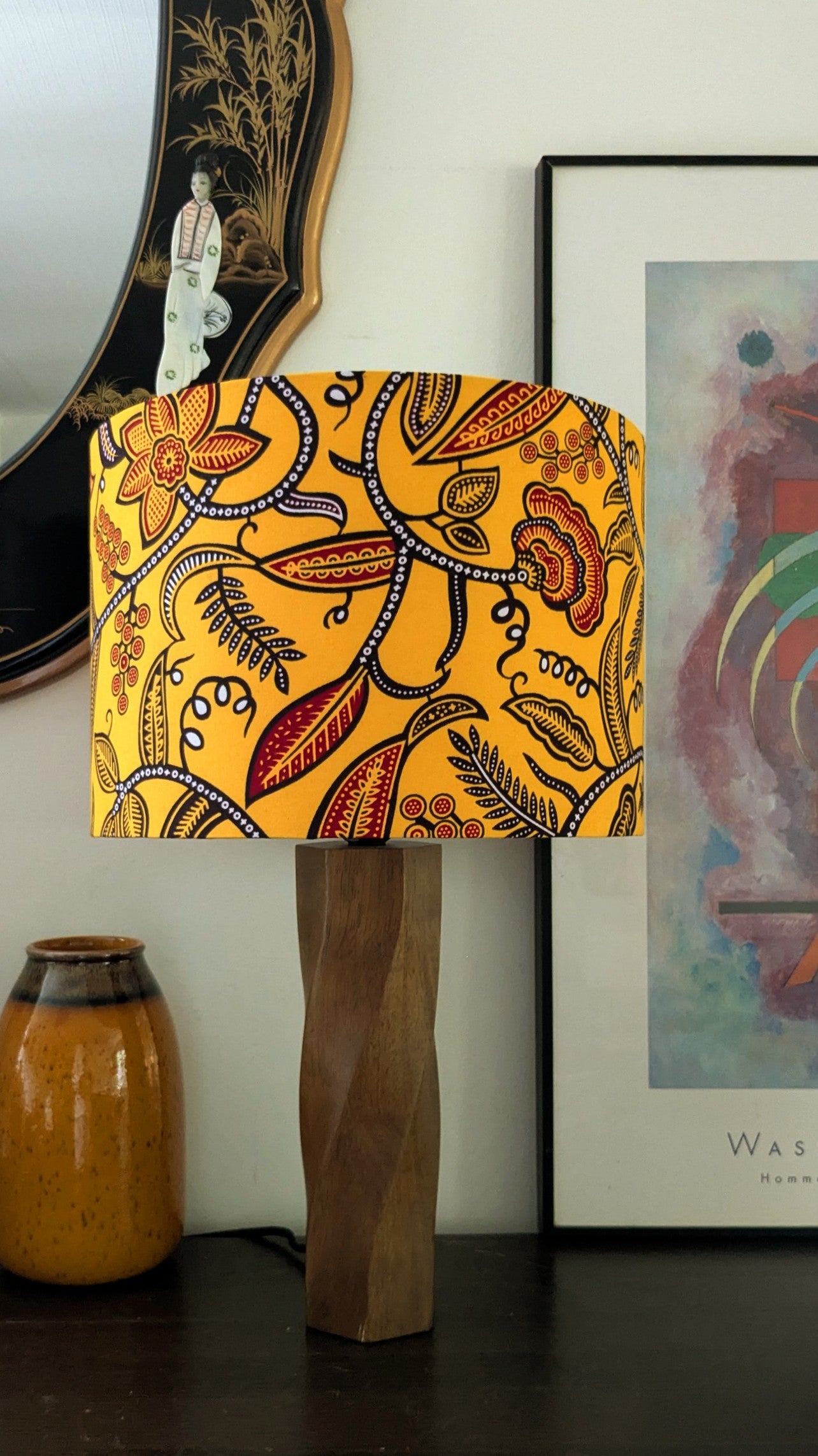 Lamp with a colorful floral patterned shade on a wooden base, against a wall with decor items.