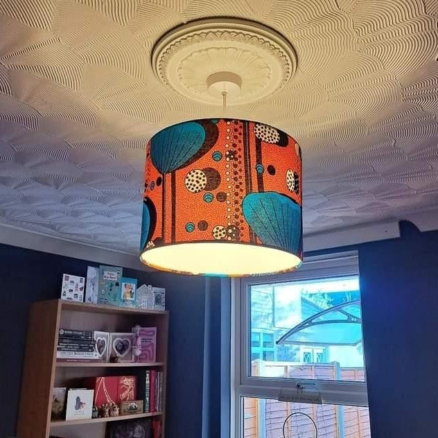 Large Orange pendant lampshade hanging from the ceiling. It has large turquoise poppy flower pattern. The light is switched on. 