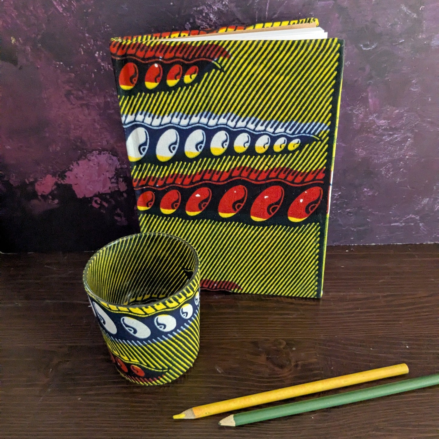 Colorful notebook and candle holder with abstract designs on a wooden surface