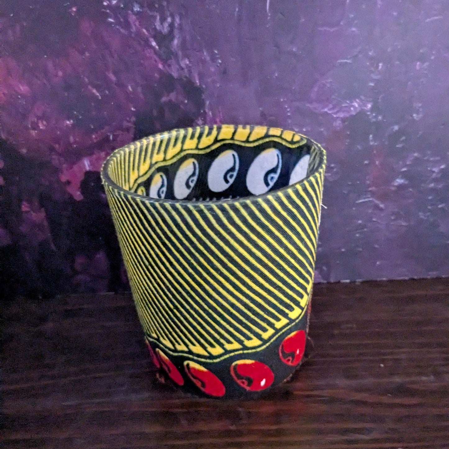 Decorative candle holder with black and red design on a wooden surface