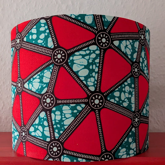 Colorful drum lampshade with geometric patterned triangles on a red surface