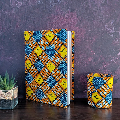 Notebook and candle holder with colorful criss cross geometric block pattern on a dark surface and purple background