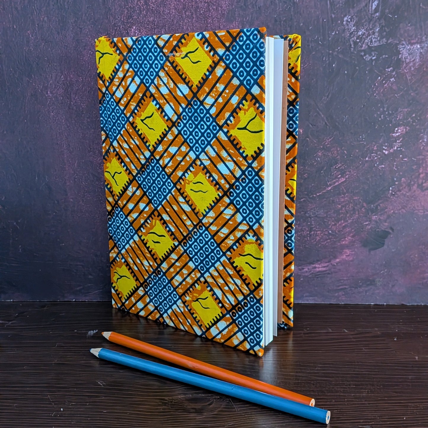 Notebook with a colorful geometric  pattern on a dark surface with two pencils.